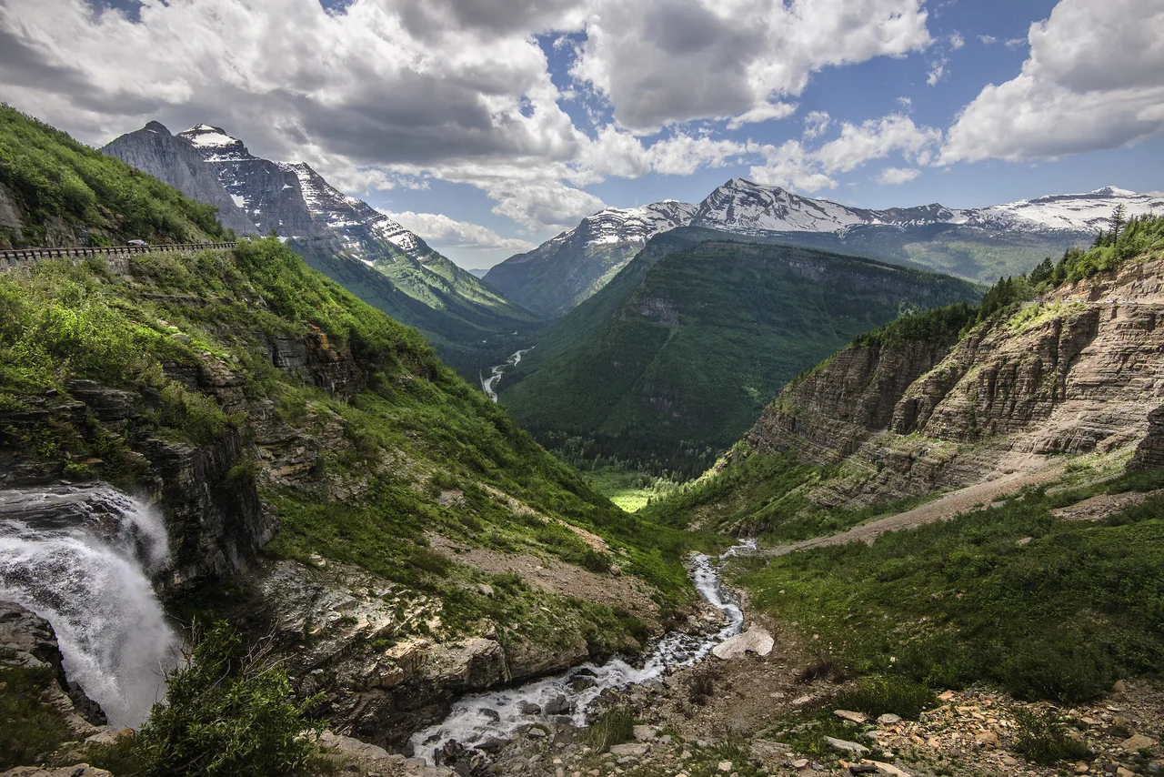 Going to the Sun Road carved along a cliff above a waterfall and sweeping glacier valley