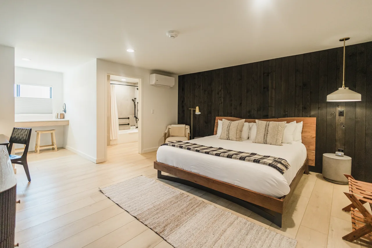 King ADA room wide view: walnut bed, dark shiplap accent wall, pendant light, and open bathroom entry