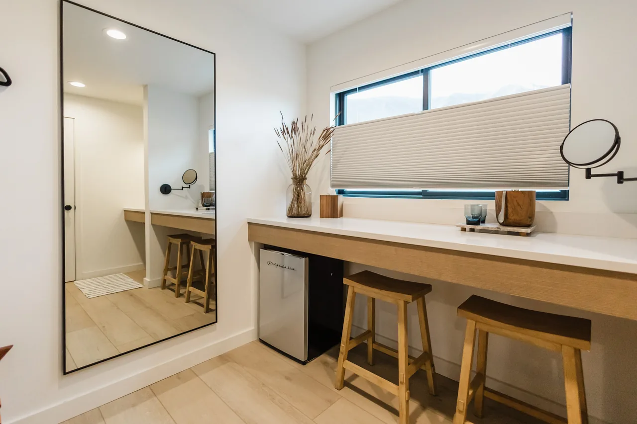 Bright dressing area with full-length mirror, warm wood counter, bar stools, and mini-fridge
