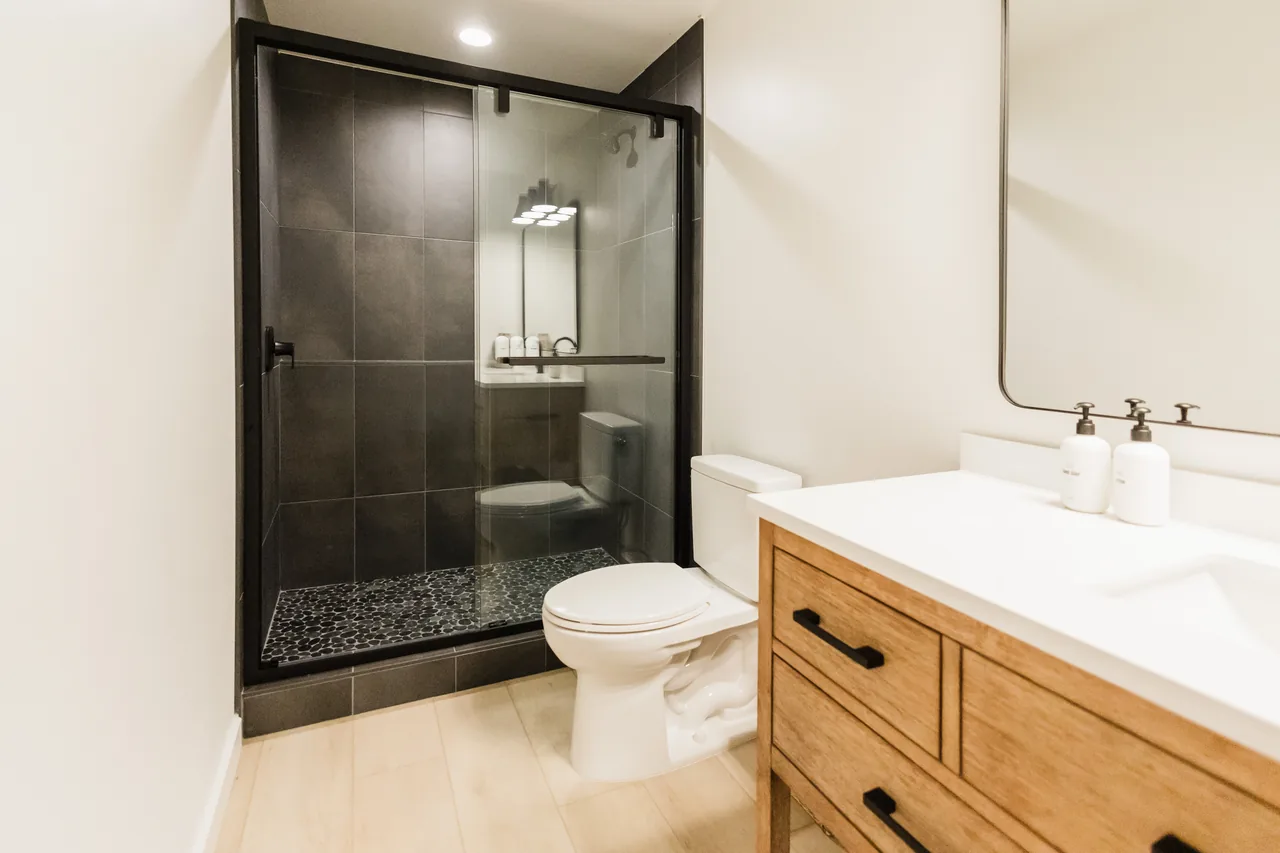 Bathroom with black-framed glass walk-in shower, warm wood vanity, white quartz countertop, and black fixtures