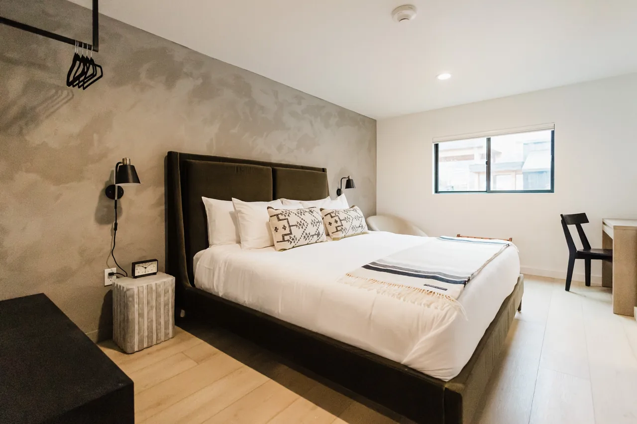 King micro room with dark velvet headboard, textured plaster accent wall, and warm hardwood floors