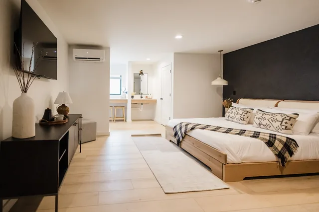 Spacious king suite with warm oak bed frame, dark accent wall, plaid throw, and open vanity alcove beyond