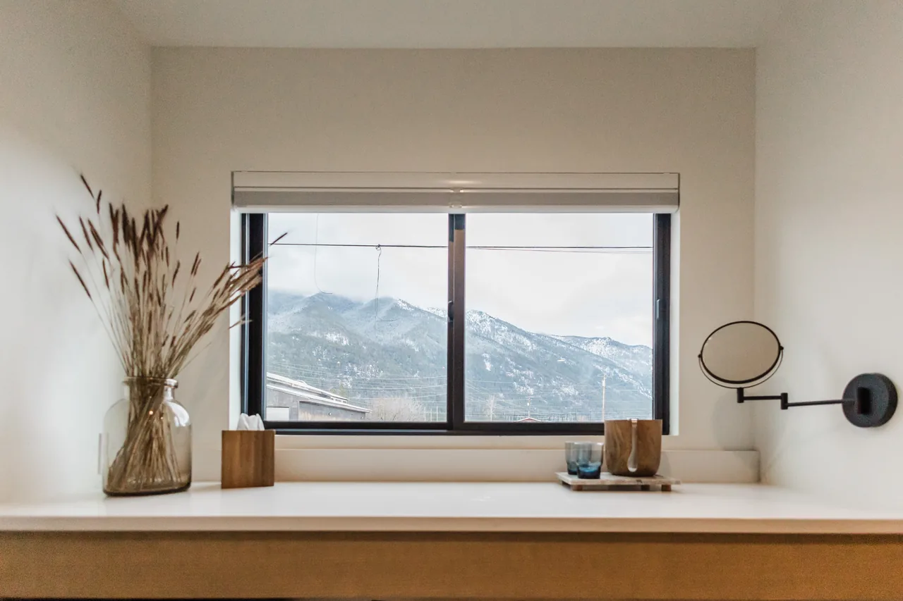 Vanity shelf with dried grasses and mountain view framed in a black-trim window with snow-capped peaks beyond