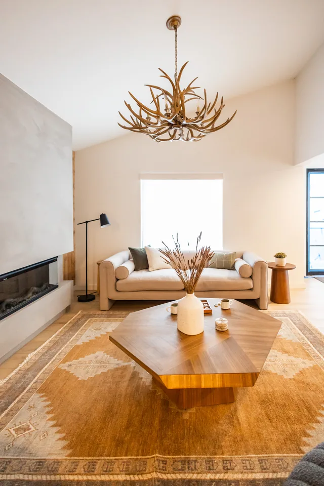 Centered lobby view of plaster fireplace flanked by cream sofa and walnut coffee table beneath antler chandelier