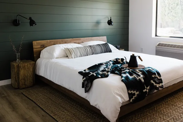 King bed with forest-green shiplap headboard wall, Pendleton throw, and wood-stump nightstand