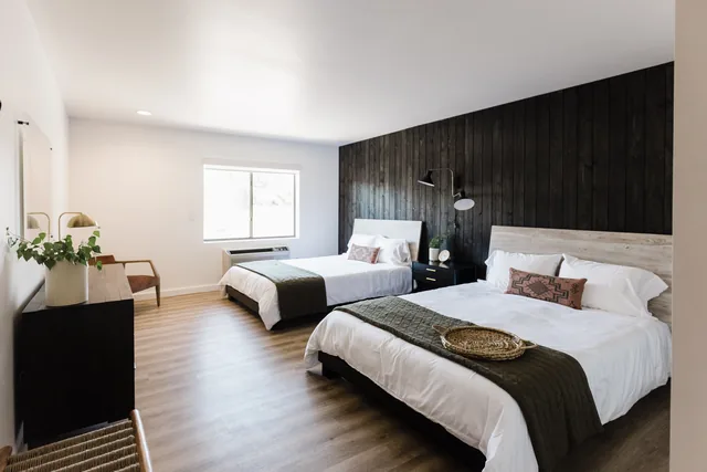 Spacious double-queen room with charcoal shiplap wall, white linens, and warm wood floors