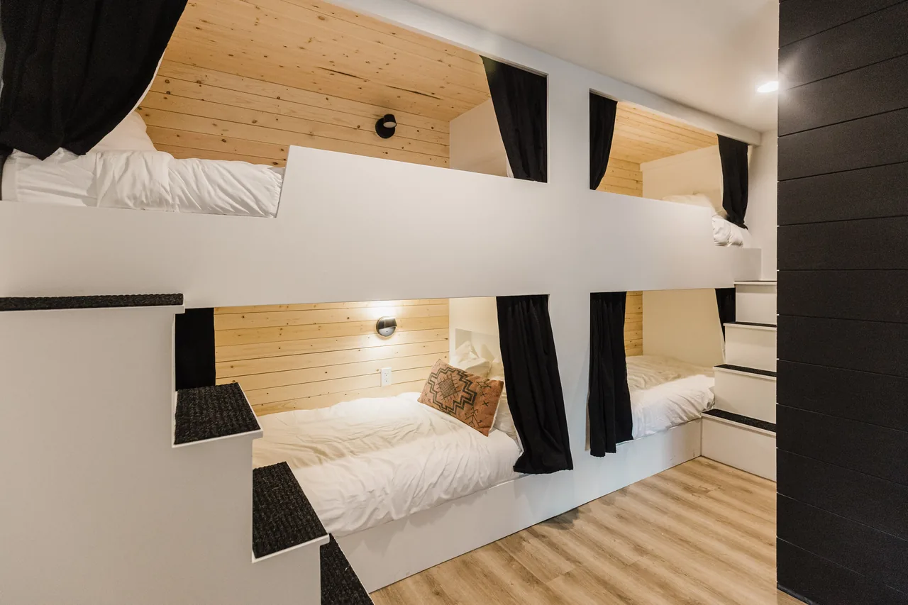 Custom bunk room with white pod bunks, black privacy curtains, pine shiplap walls, and warm accent lighting