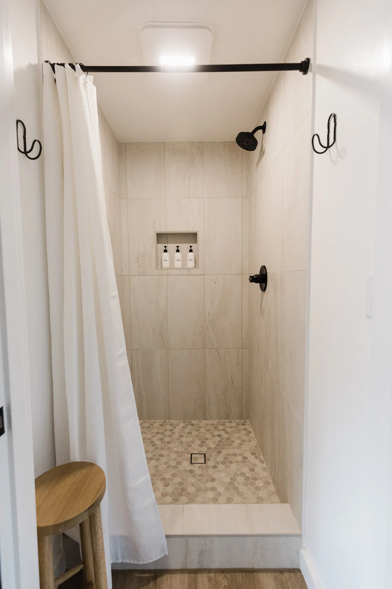Clean walk-in shower with large-format stone tile, matte-black rainfall head, built-in toiletry niche, and pebble floor
