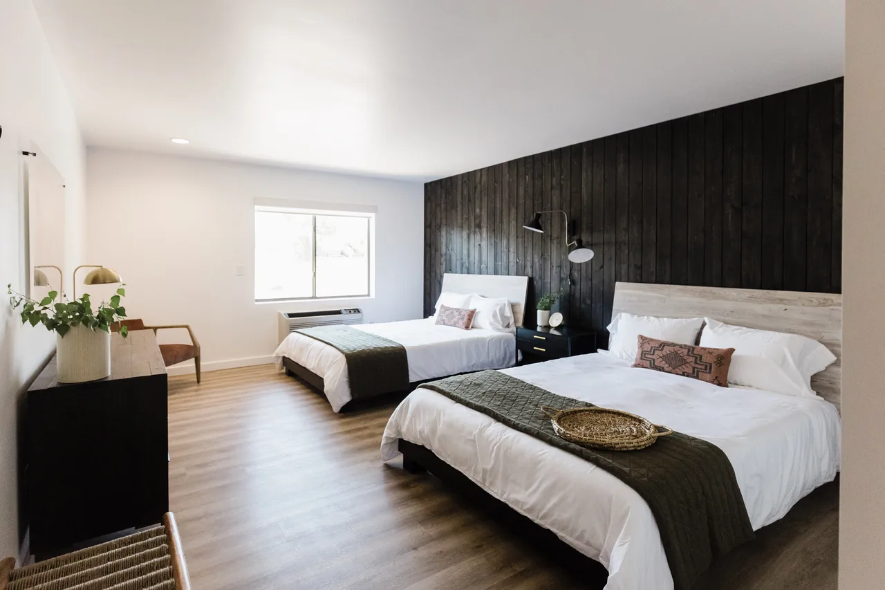 Bright double queen room with charcoal shiplap accent wall, two crisp white beds, brass sconces, and warm wood floors