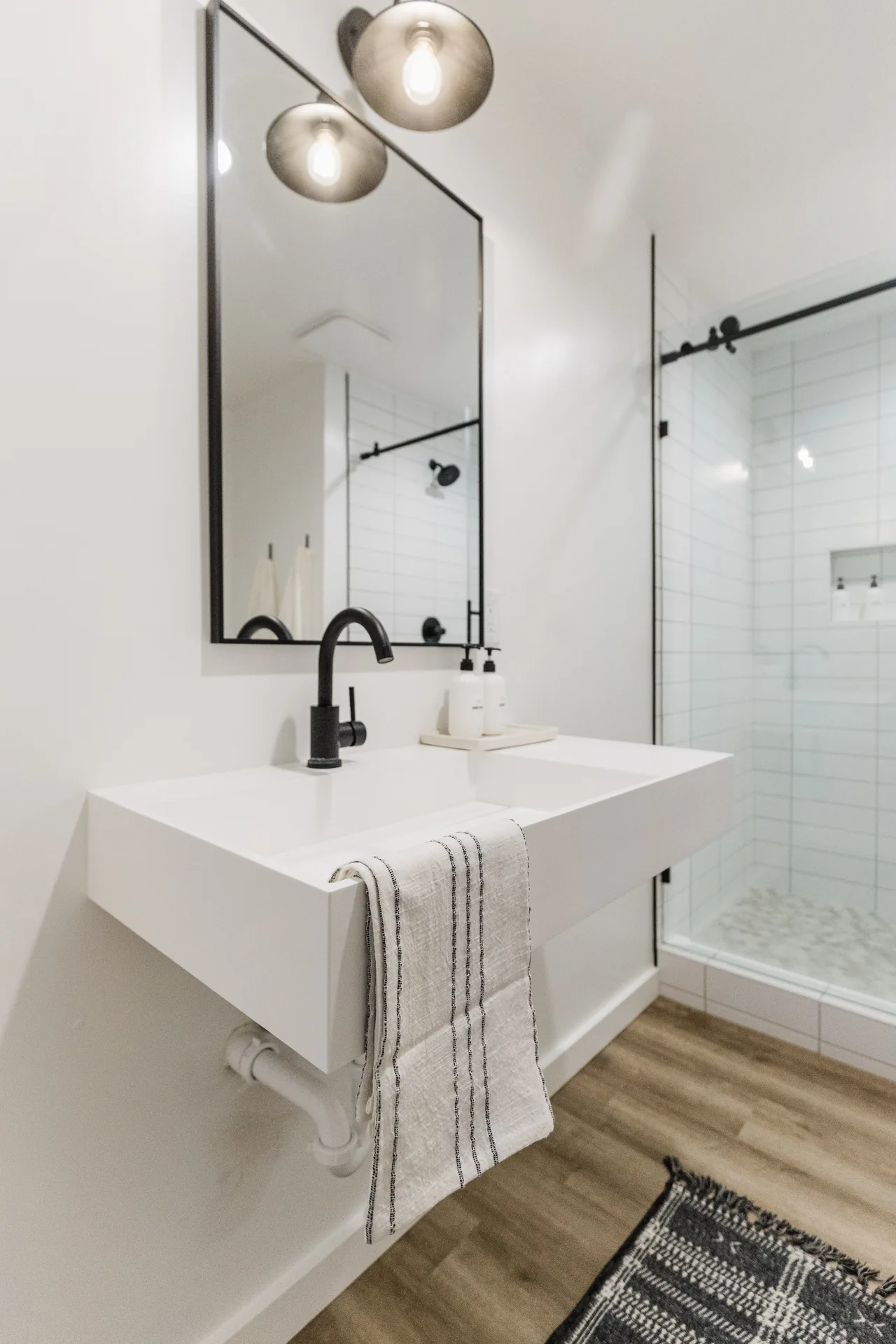 Floating white vanity with matte-black faucet, globe pendant lights, and walk-in glass shower reflected in mirror