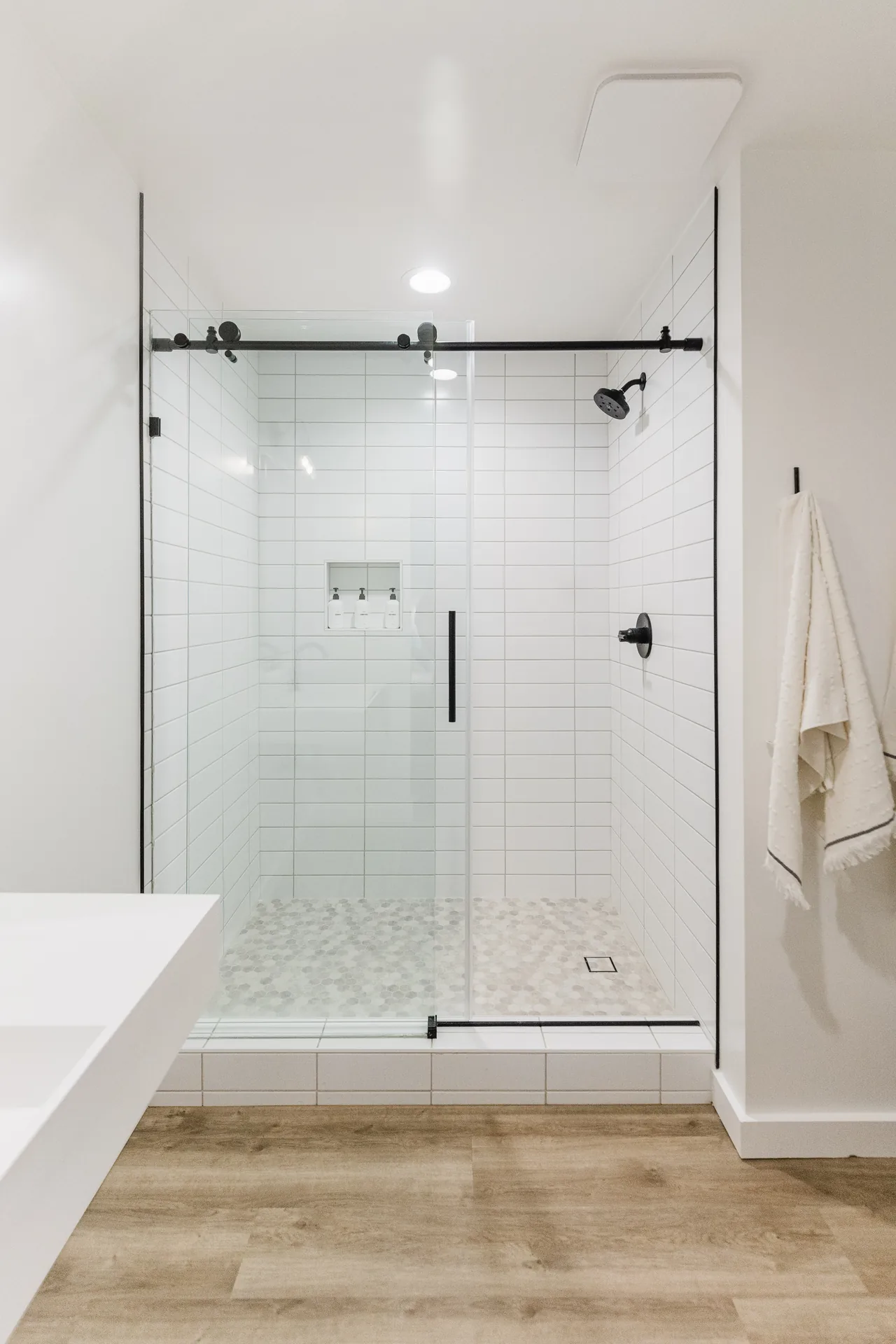 Walk-in glass shower with white subway tile, hexagon marble floor, and matte-black barn-door hardware