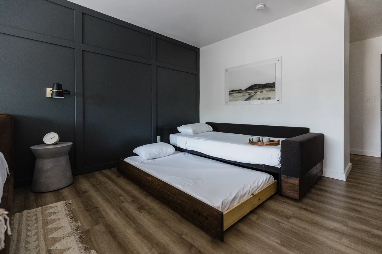 Trundle bed pulled out beside daybed sofa, dark accent wall, local landscape artwork above