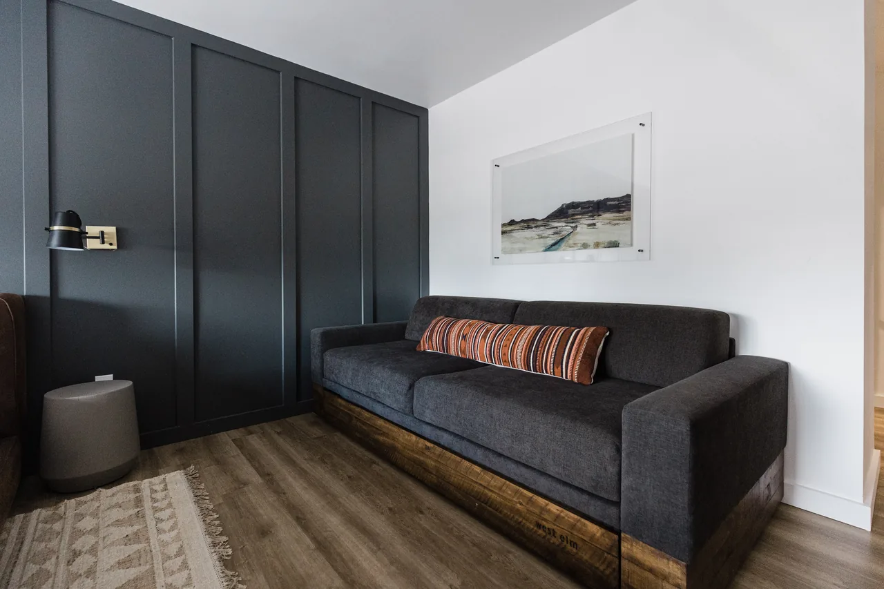 Charcoal daybed sofa with striped accent pillow, reclaimed-wood base, local landscape art, dark paneled wall