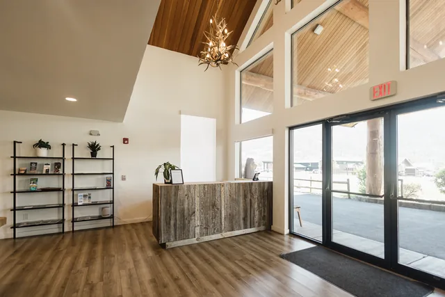 Reclaimed-wood front desk beneath an antler chandelier with floor-to-ceiling windows overlooking the Montana landscape