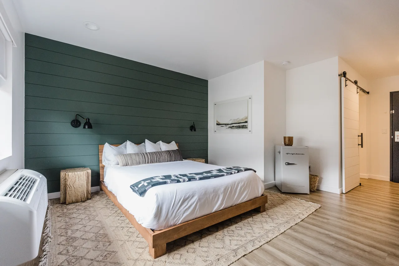 Queen ADA room with deep forest-green shiplap accent wall, wooden platform bed, white linens, and barn door entry