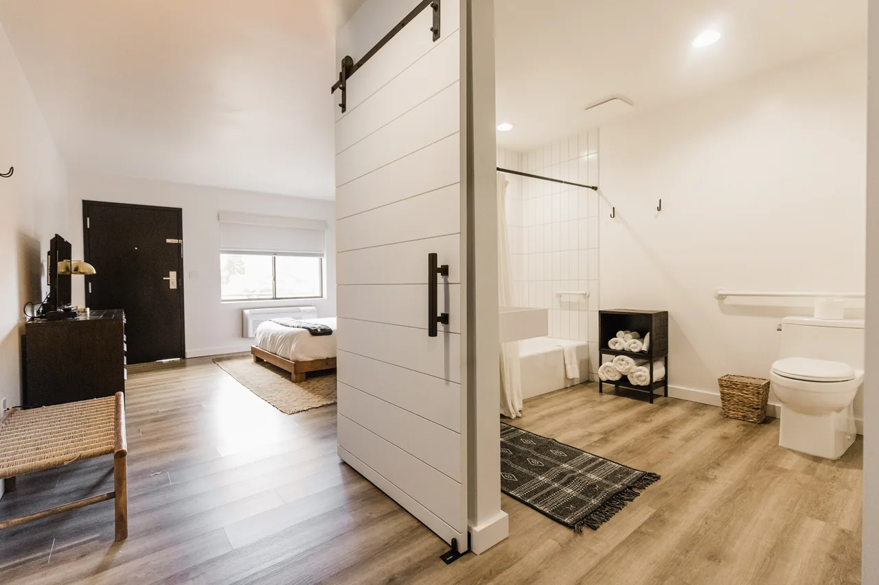 Open barn door revealing ADA bathroom alongside the bedroom — showing the full room layout and shiplap divider