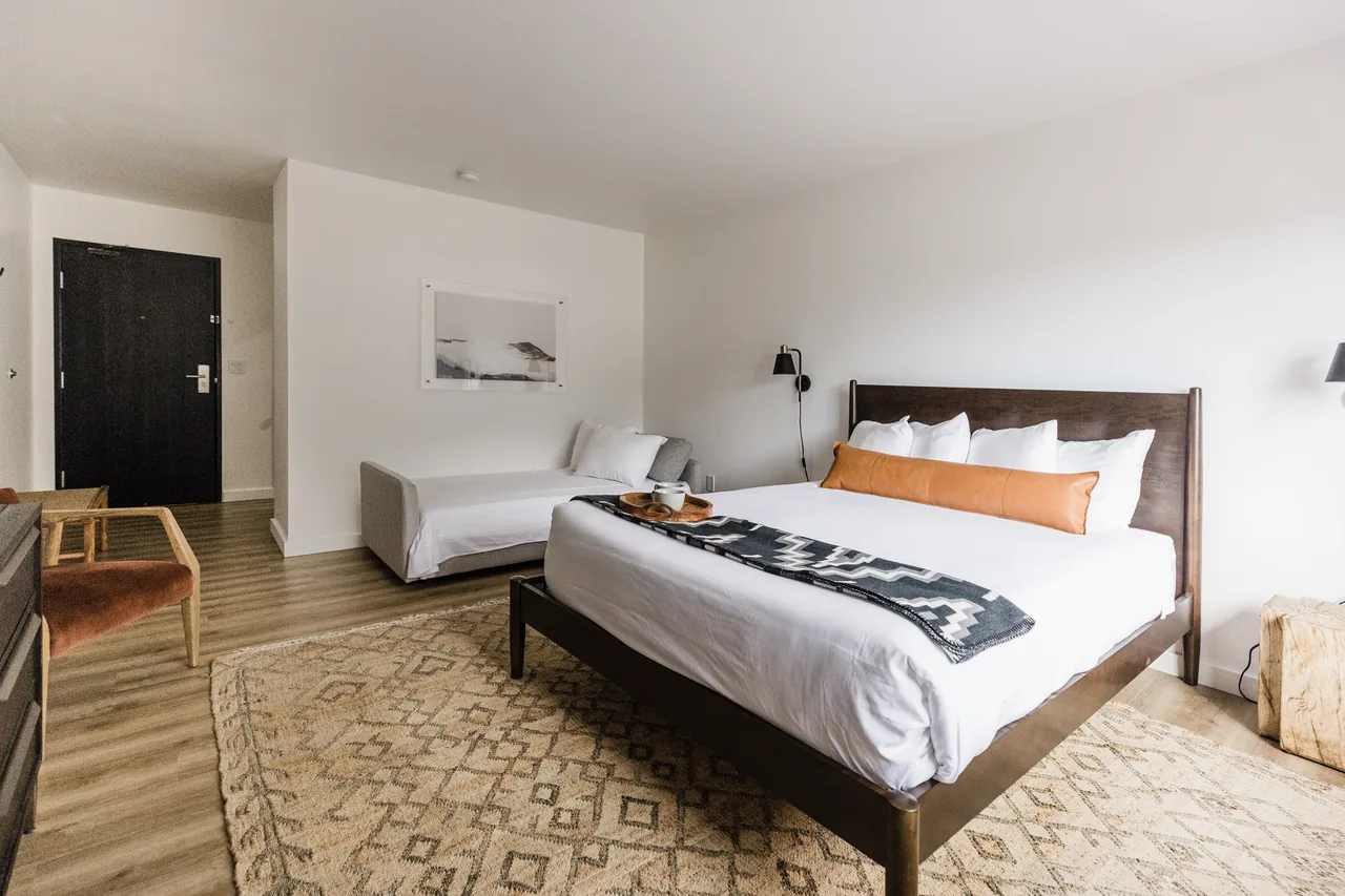 Bright queen bedroom with walnut bed frame, leather lumbar pillow, Navajo throw, sofa sleeper, and woven rug