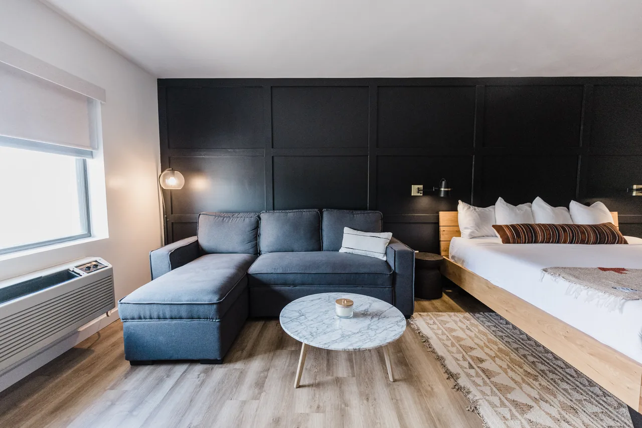 Suite sitting area with navy sectional sofa, marble coffee table, and king bed against black accent wall